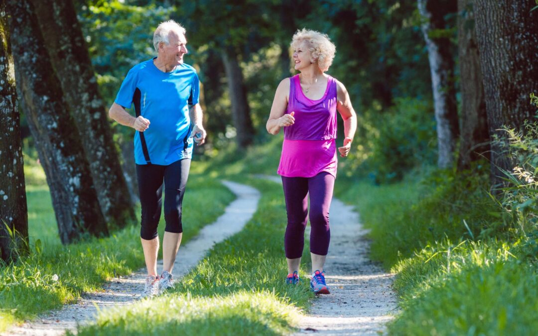 Older couple jogging on a trail through the woods on a warm day
